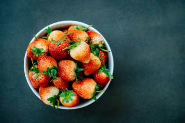 Siyah taş zemin üzerine beyaz kase çilek meyve