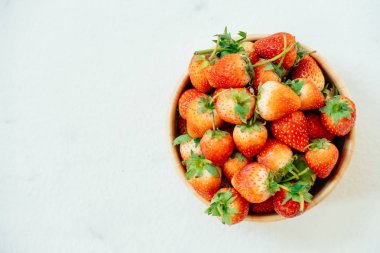 Beyaz taş zemin üzerine ahşap kase çilek meyve