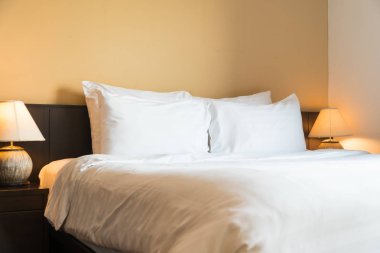 Yatak odasının içinde lamba süslemesi olan beyaz rahat bir yastık.