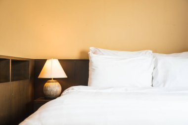 Yatak odasının içinde lamba süslemesi olan beyaz rahat bir yastık.