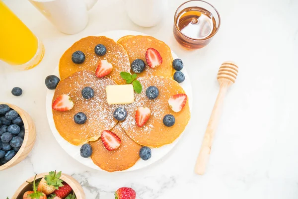 健康早餐配有煎饼蓝莓和草莓水果 黑咖啡 牛奶和橙汁在白色的石头桌背景 — 图库照片