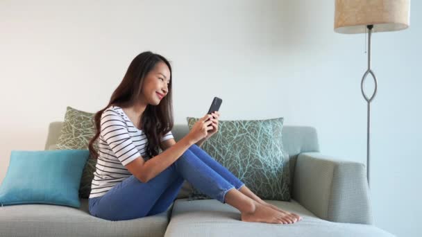 아름다운 아시아 혼자서 집에서 소파에서 스마트폰을 사용하고 — 비디오