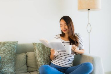 Kahve küpüyle kitap okuyan güzel Asyalı genç kadınların portresi.