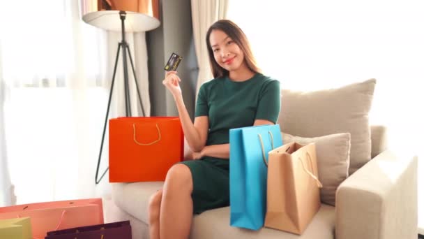 美丽的亚洲女人坐在沙发上 提着购物袋和信用卡的镜头 — 图库视频影像