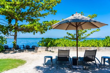 Şemsiye ve sandalye kumsalda ve denizde mavi gökyüzüyle