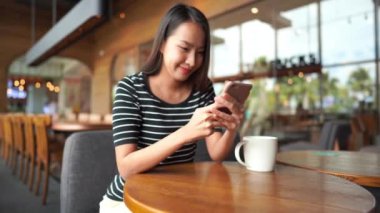 Güzel bir Asyalı kadının restoranda oturup akıllı telefon kullandığının görüntüleri.