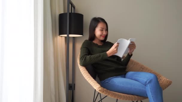 自宅でソファで本を読んでいる美しいアジア人女性の映像 — ストック動画