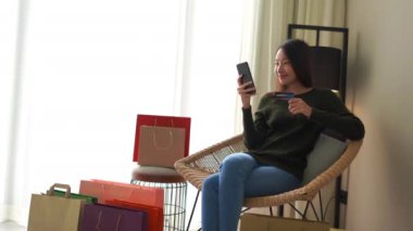 Güzel Asyalı kadının evde akıllı telefonuyla e-alışveriş yaptığı görüntüler.