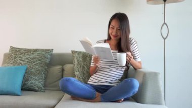 Güzel Asyalı kadının kitap okuduğu ve evde çay içtiği görüntüler.
