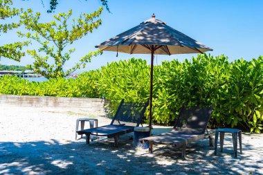 Şemsiye ve sandalye kumsalda ve denizde mavi gökyüzüyle