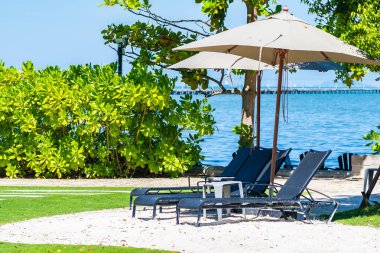 Şemsiye ve sandalye kumsalda ve denizde mavi gökyüzüyle