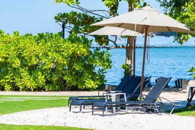 Şemsiye ve sandalye kumsalda ve denizde mavi gökyüzüyle