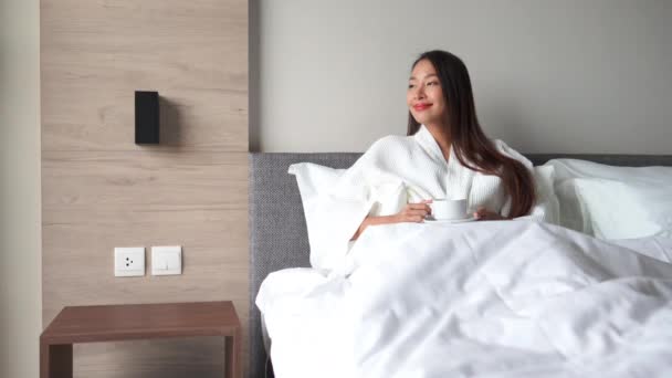 穿着浴衣的漂亮亚洲女人在床上喝咖啡的镜头 — 图库视频影像