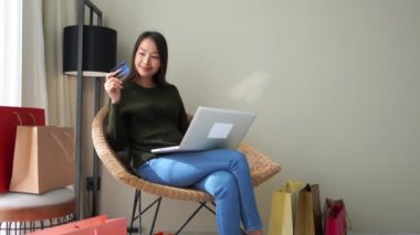Asyalı bir kadının evde dizüstü bilgisayarla e-alışveriş yaptığını gösteren görüntüler.