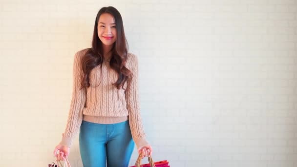 美丽的亚洲女人带着购物袋站在白墙前的镜头 — 图库视频影像