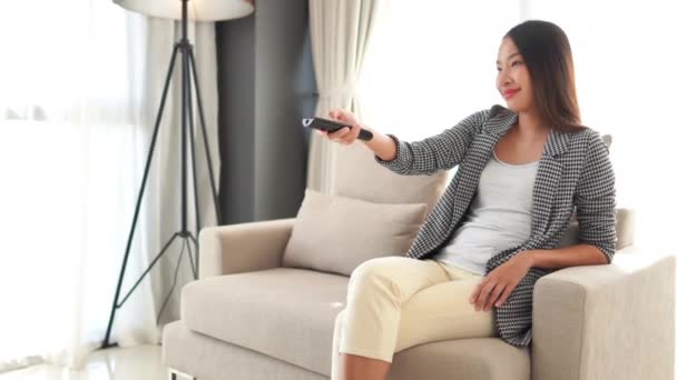 美丽的亚洲女人在家里用遥控器看电视的镜头 — 图库视频影像