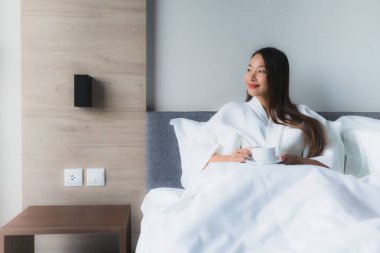 Yatağında kahve fincanı olan güzel Asyalı genç kadınların portresi.