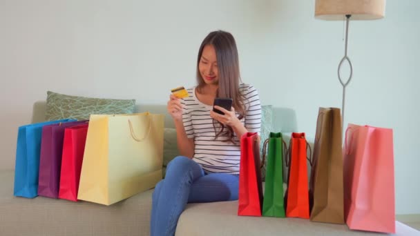 美しいアジアの女性が自宅でスマートフォンでEショッピングをしている様子 — ストック動画