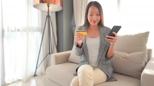 美しいアジアの女性が自宅でスマートフォンでEショッピングをしている様子 — ストック動画
