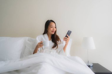 Kahve fincanı ve cep telefonuyla güzel Asyalı genç kadınların portresi. 
