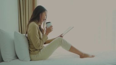 Evde kitap okuyan güzel Asyalı kadının görüntüleri.