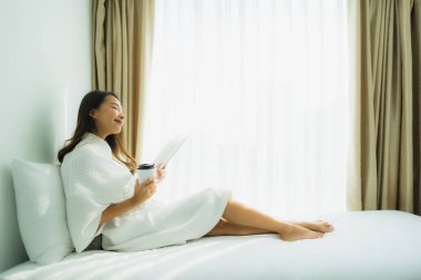 Elinde kahve fincanı olan ve kitap okuyan Asyalı genç bir kadın.