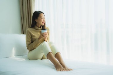 Yatağında kahve fincanı olan Asyalı genç bir kadın.