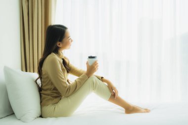 Yatağında kahve fincanı olan Asyalı genç bir kadın.