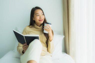 Elinde kahve fincanı olan ve kitap okuyan Asyalı genç bir kadın.