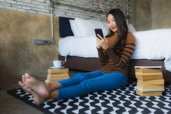 Молода азіатська жінка використовує смартфон з читанням книги і спільно — стокове фото