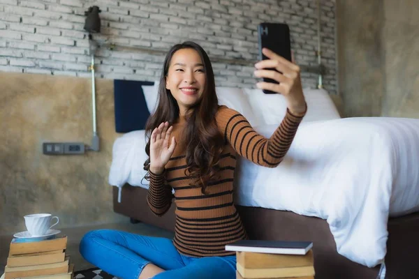 Ung asiatisk kvinna som använder smart mobiltelefon med läsa bok och co — Stockfoto