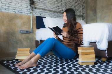 Elinde kahve fincanı olan ve kitap okuyan Asyalı genç bir kadın.