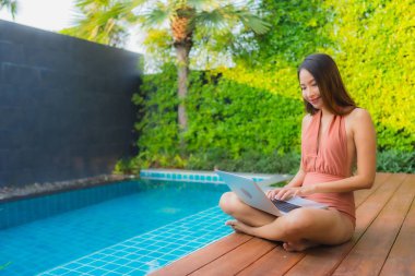 Dışarıda dizüstü bilgisayar kullanan Asyalı genç bir kadının portresi. 