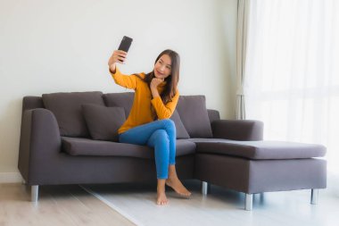 Kanepede akıllı cep telefonu kullanan Asyalı genç bir kadının portresi.