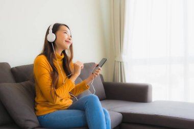 Genç Asyalı kadının portresi kulaklıklı akıllı cep telefonu kullanıyor.