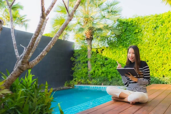 Portrait young asian woman read book around outdoor swimming poo