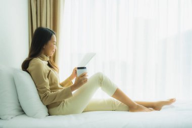 Elinde kahve fincanı olan ve kitap okuyan Asyalı genç bir kadın.