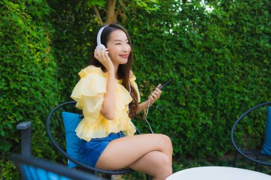 Genç Asyalı kadın Li için kulaklıklı akıllı cep telefonu kullanıyor.