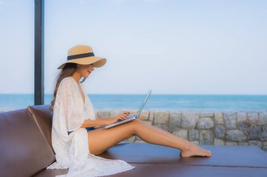 Plaj çevresinde dizüstü bilgisayar kullanan Asyalı genç bir kadının portresi.