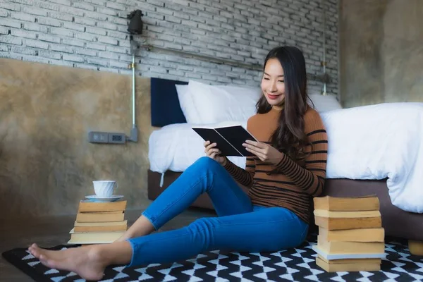 Elinde kahve fincanı olan ve kitap okuyan Asyalı genç bir kadın. — Stok fotoğraf