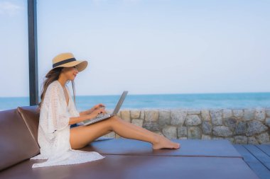 Plaj çevresinde dizüstü bilgisayar kullanan Asyalı genç bir kadının portresi.