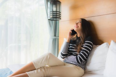 Yatakta akıllı cep telefonu kullanan Asyalı genç bir kadının portresi