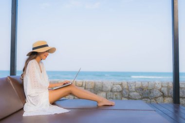 Plaj çevresinde dizüstü bilgisayar kullanan Asyalı genç bir kadının portresi.