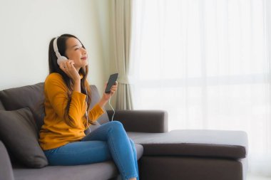 Genç Asyalı kadının portresi kulaklıklı akıllı cep telefonu kullanıyor.