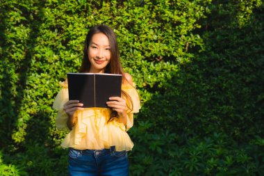 Genç Asyalı kadın açık hava bahçesinde kitap okuyor.
