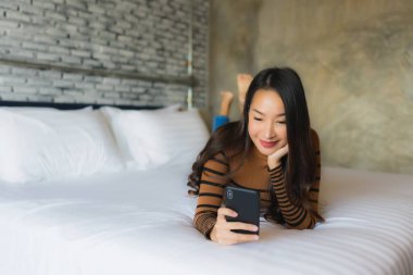 Genç Asyalı kadın yatakta cep telefonu kullanıyor.