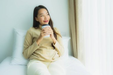 Yatağında kahve fincanı olan Asyalı genç bir kadın.