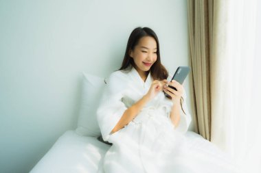Genç Asyalı kadın yatakta cep telefonu kullanıyor.