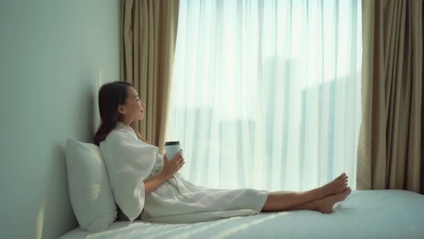隔離中に自宅でベッドの上でリラックスしたバスローブの美しいアジア人女性の映像 — ストック動画