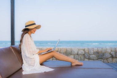 Plaj çevresinde dizüstü bilgisayar kullanan Asyalı genç bir kadının portresi.